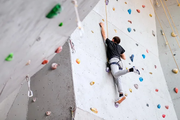 Man climbing on artificial boulders wall indoor, rear view