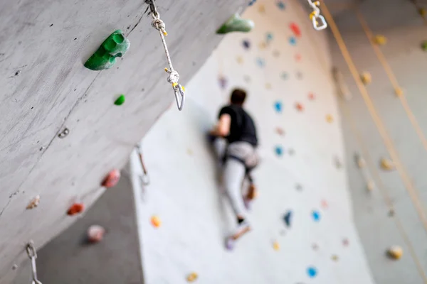 Man climbing on practical wall indoor, securing carabiners and rope