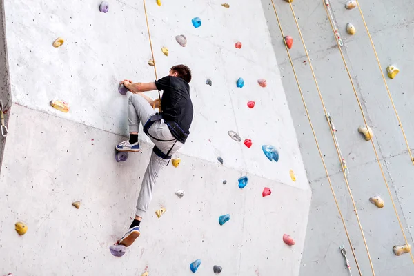 Man climbing on artificial boulders wall indoor, rear view