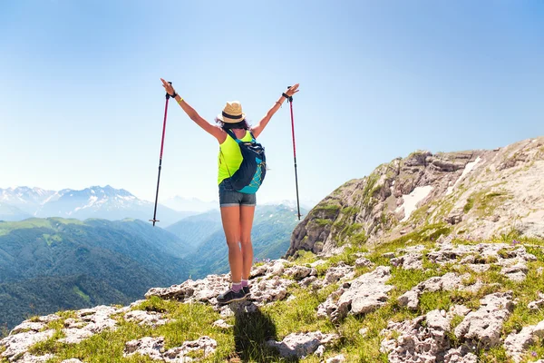 Woman hiker with trekking poles is enjoying the view from the mountains in the hat