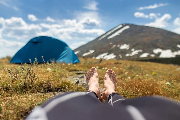 Bare feet of resting camper with tent and mountain view at backg
