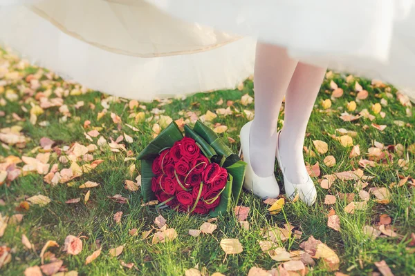 Near the feet of the bride on the grass lies wedding bouquet