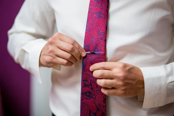 People, business, fashion and clothing concept - close up of man in shirt dressing up and adjusting purple tie with clasp