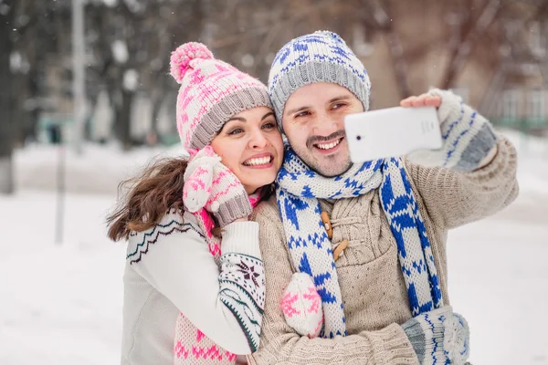 Couple in love making selfie on winter outdoors in sweaters, scarf and mittens