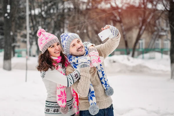 Couple in love making selfie on winter outdoors in sweaters, scarf and mittens