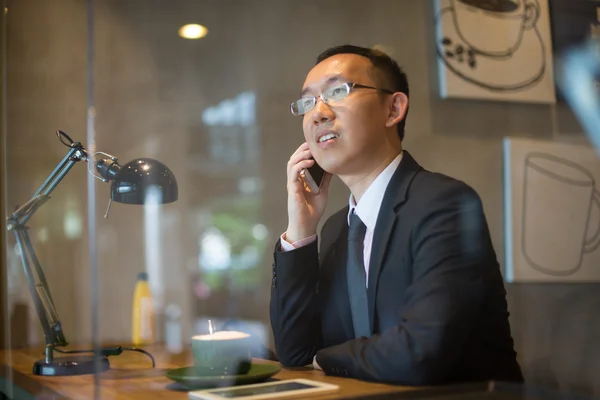Asian business man having coffee and phone conversation at cafe