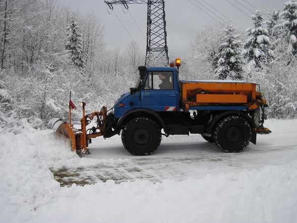 Machinery with snowplough cleaning road by removing snow from in