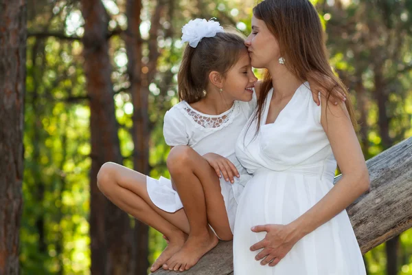 Happy pregnant mother  kissing her daughter outdoors