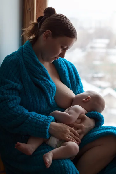 Woman breastfeeding her baby near a window, color image