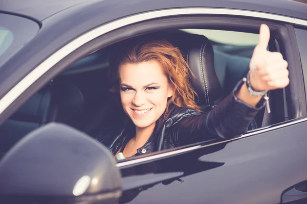 Young happy woman showing Ok sign, thumb up in a sport car