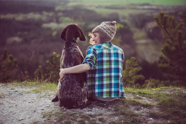 Woman and her dog posing outdoor. Girl loving and hugging tightly her dog and watching landscape.