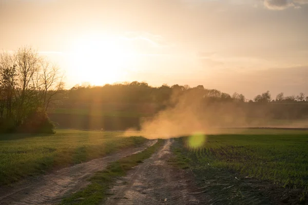 Country road landscape in sunset. Sun rays through the dust.