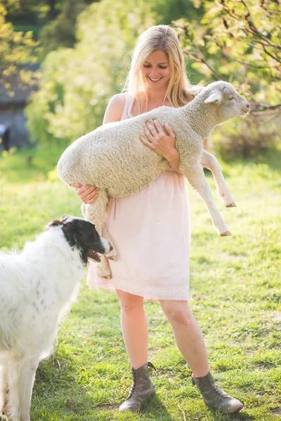 Blonde farmer woman holding a lamb outdoor. Farm living concept.