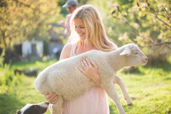 Blonde farmer woman holding a lamb outdoor. Farm living concept.