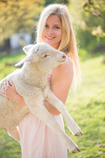 Blonde farmer woman holding a lamb outdoor. Farm living concept.