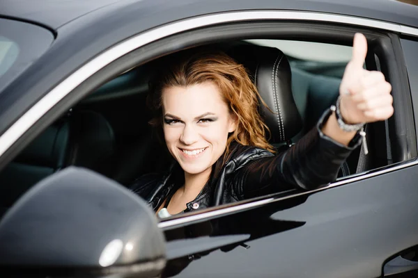 Woman in black sport car showing OK sign, thumb up