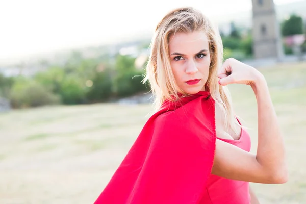 Confident blonde woman in red costume showing muscle and strength