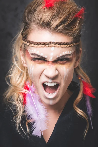 American Indian warrior with paint face camouflage, screaming with mouth open - studio photo with professional makeup