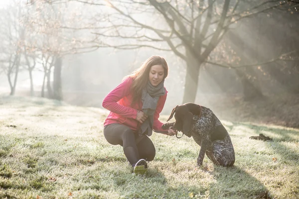 Woman and her dog stretching outdoor. Fitness girl and her pet working out together.