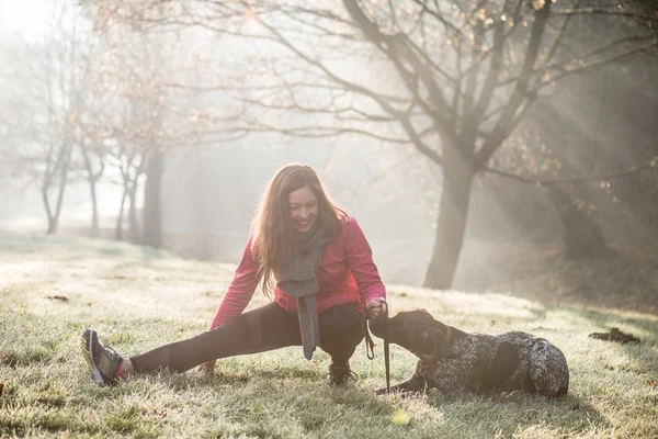 Woman and her dog stretching outdoor. Fitness girl and her pet working out together.