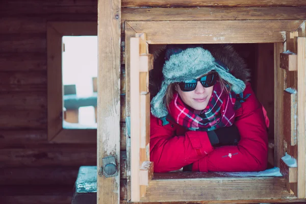 Young woman looking out a window on ski vacation in a wooden house.