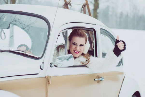 Young woman driving vintage car at snowy road. Happy caucasian woman driving a VW beetle car.