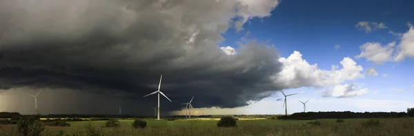 Panorama of windmills on rural field in the storm clouds and rain. Wind turbines panorama in countryside.
