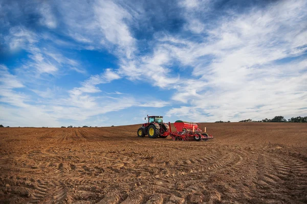 Farmer with tractor seeding crops at field