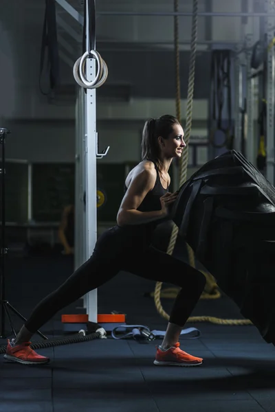 Powerful muscular woman CrossFit trainer doing tire workout at gym