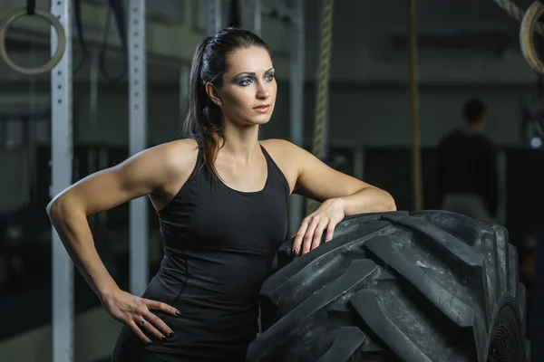 Powerful muscular woman CrossFit trainer doing tire workout at gym