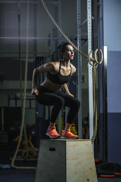 Powerful muscular woman CrossFit trainer jumps during workout at gym