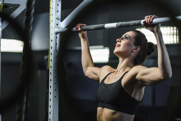 Powerful attractive woman CrossFit trainer do pull ups during workout