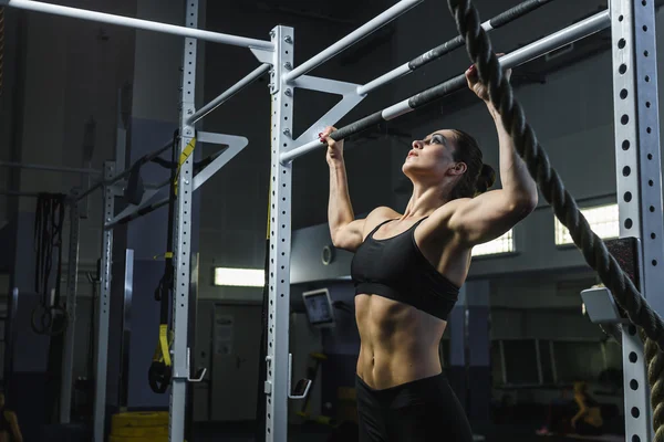 Powerful attractive woman CrossFit trainer do pull ups during workout