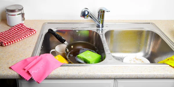 Hands washing dishes with running water from faucet