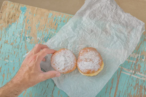 Hand reaches for sweet sugary donut on rustic table