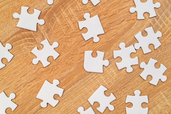 White jigsaw puzzle pieces scattered on wooden table