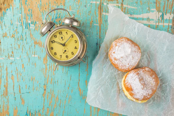 Sweet sugary donuts and vintage clock on rustic table