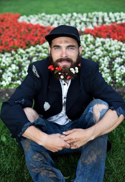 Bearded vagrant sitting in flowerbed