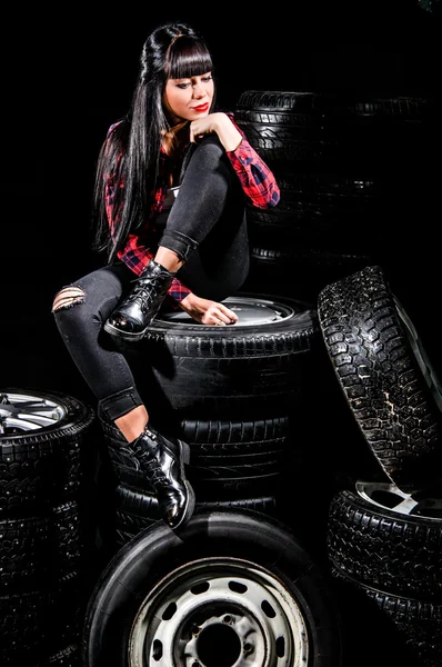 Young woman in a red checked shirt sitting on a tires