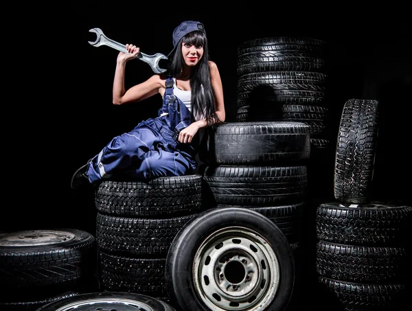 Sexy young woman sitting on wheels with a big wrench