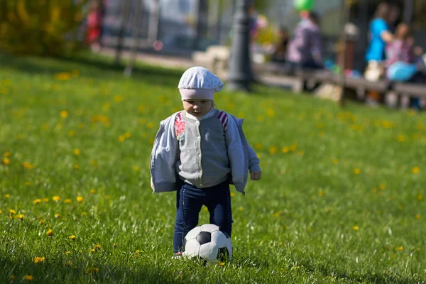 Little girl baby blond  Outdoors. Active football fan running on the green grass field with ball