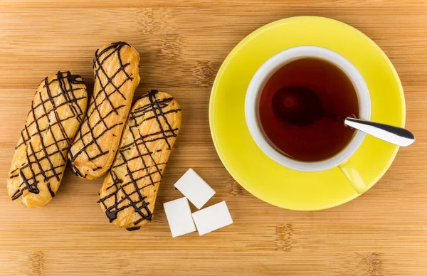 Eclairs, black tea in cup and lumpy sugar on table