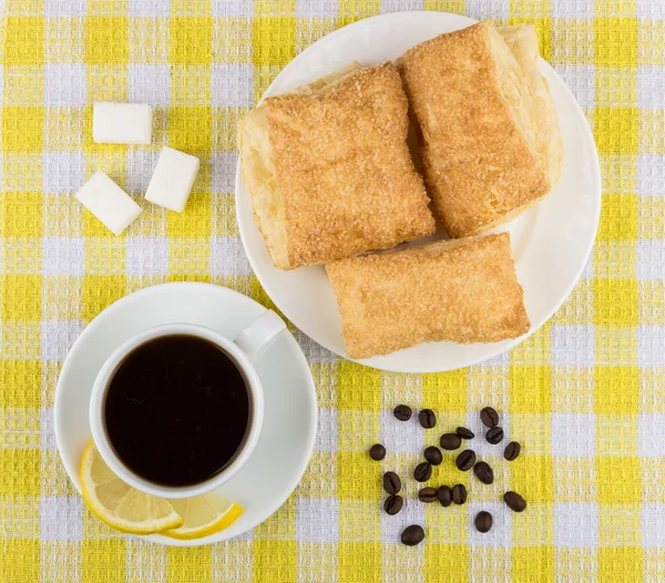 Coffee, lemon and sugar, plate with flaky biscuits on tablecloth