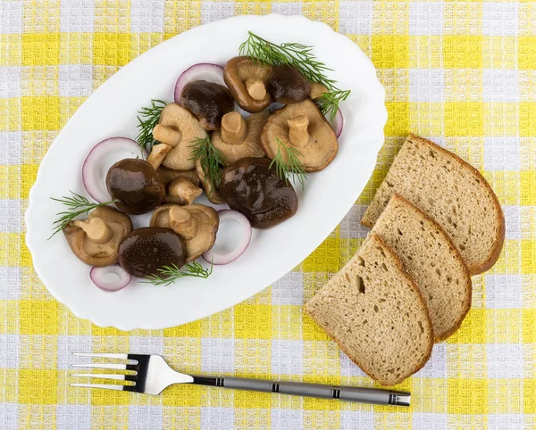 Marinated mushrooms with dill and onion in glass dish, fork