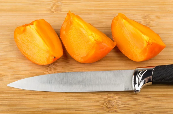 Three pieces of persimmons and knife on board