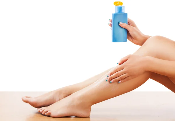 Woman sitting on the floor and apply body lotion on the leg skin.Studio shot