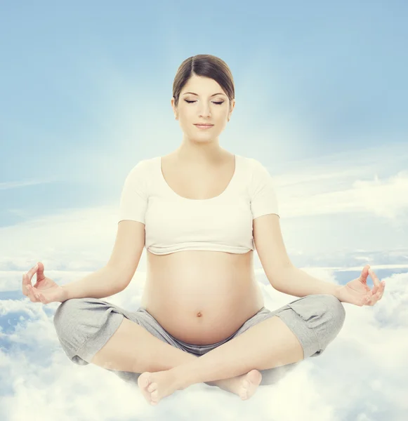 Pregnant Woman Yoga Meditation. Pregnancy Health Wellness and Relax Exercising. Mother Sitting in Lotus Position Crossed Legs over Sky Background