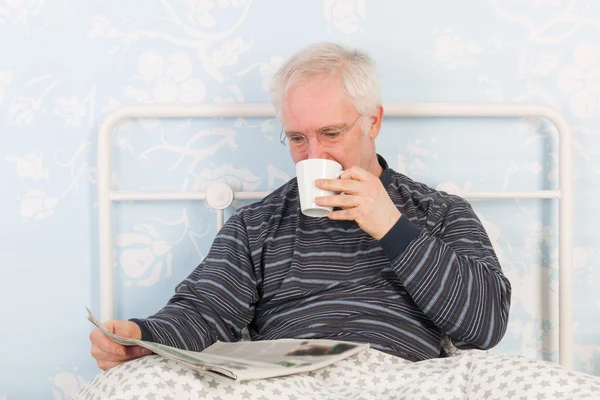 Senior man reading newspapers in bed