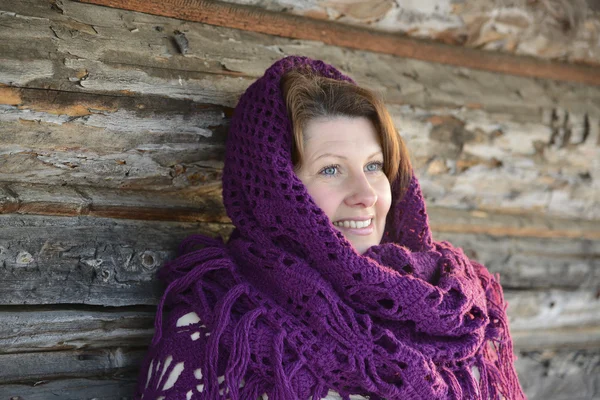 The Russian woman in  shawl warms hands near an izba