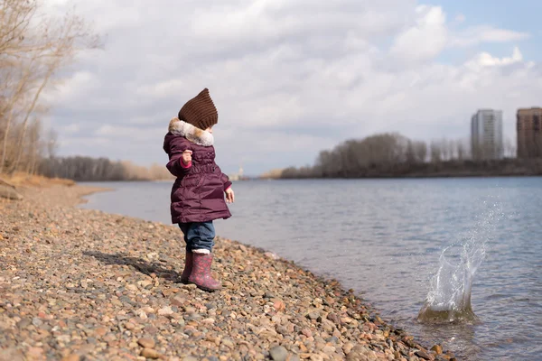 Little girl throwing a stone into river